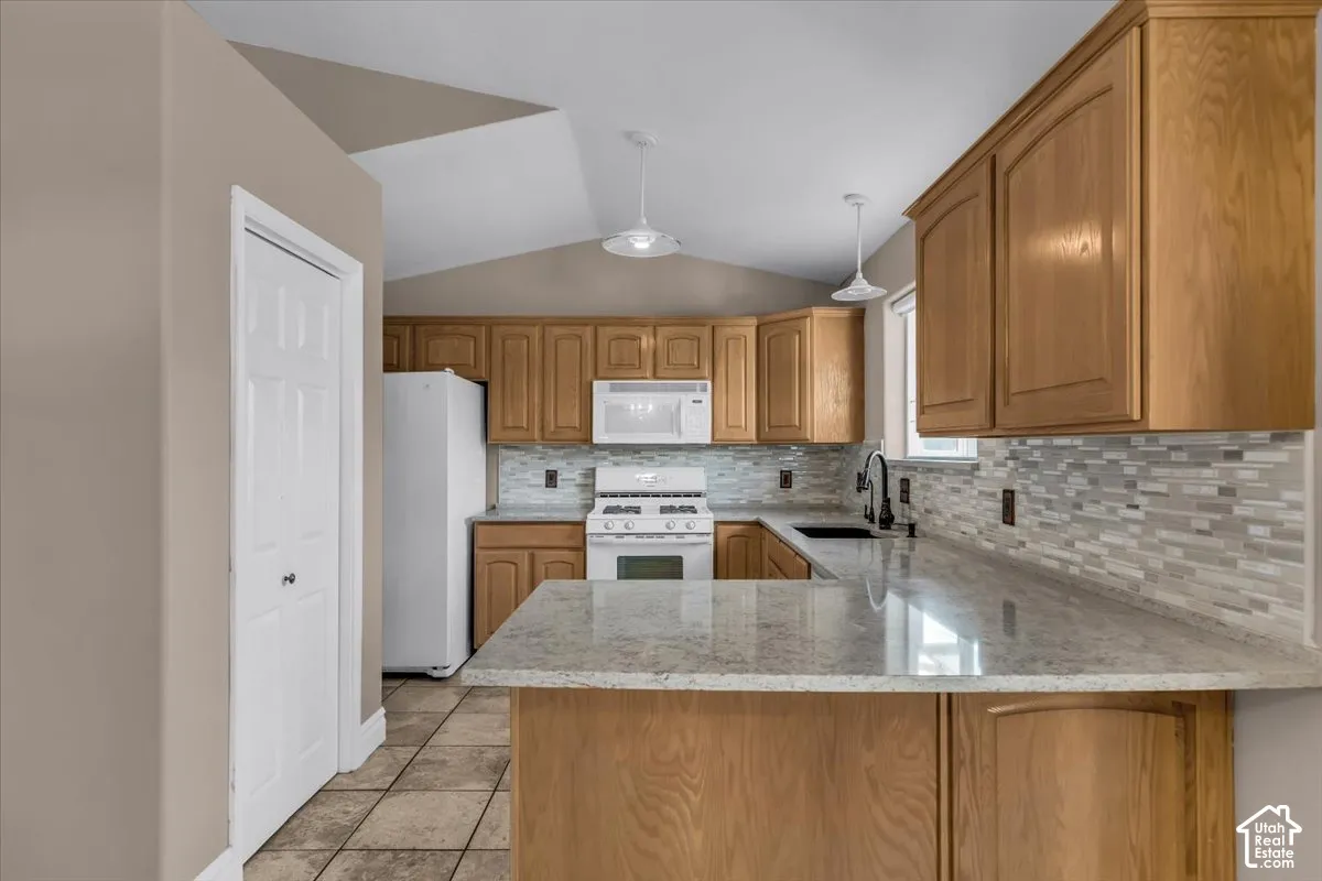 Kitchen featuring light wood cabinetry, white appliances, a tile backsplash, and a light-toned countertop