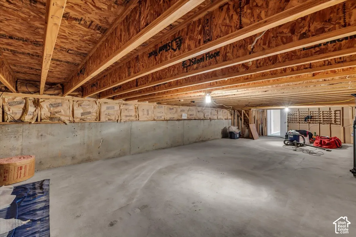 Expansive basement storage area featuring exposed wood joists, concrete foundation walls, and a concrete floor