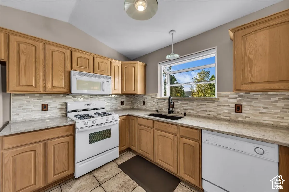 Kitchen featuring wood cabinetry, light-toned quartz countertops, a glass tile backsplash, and a box window with natural light