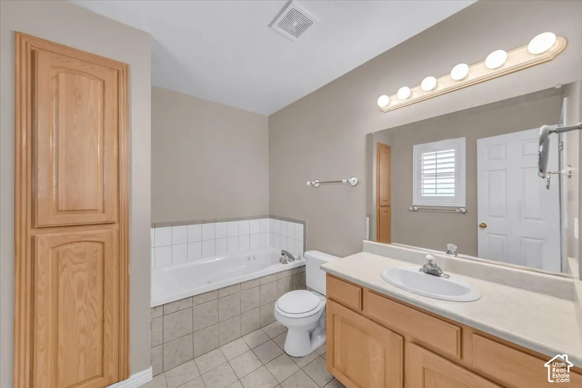 White jetted tub with tile surround, wood-finish vanity with countertop, integrated sink, and an expansive wall-mounted mirror