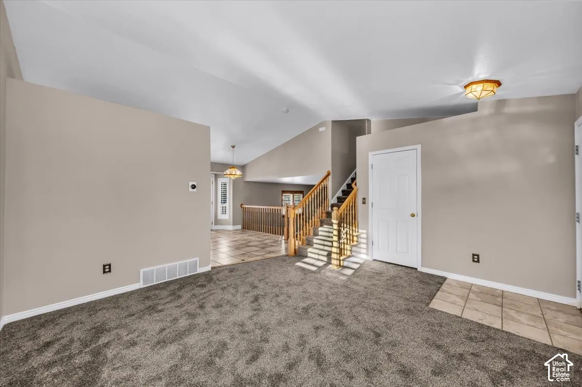 Vaulted ceilings with a flush mount light fixture, carpet flooring, a natural wood staircase with balusters, and a paneled white door