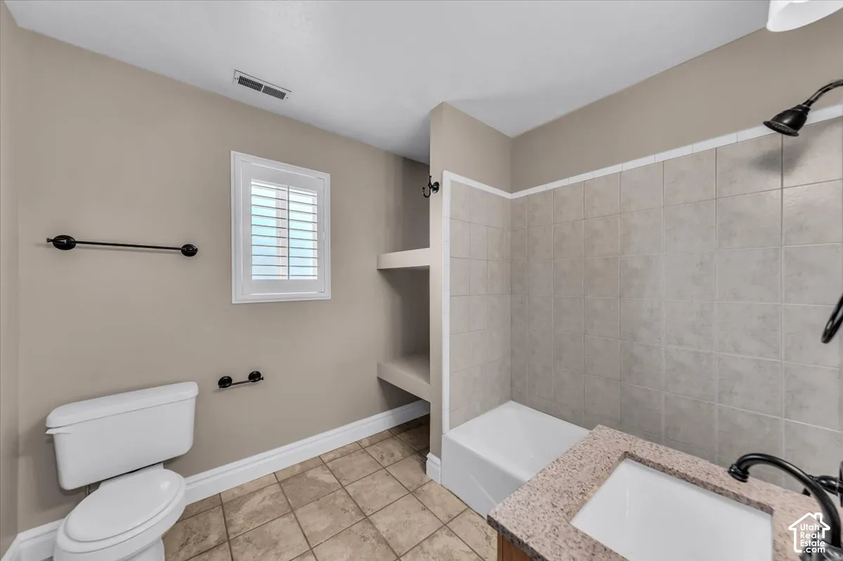 Main floor bathroom featuring a  tub/shower combination with tile surround, a vanity with a white sink and granite-style countertop, and laundry area
