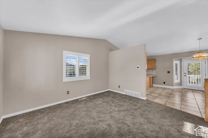 Vaulted ceiling, carpeted flooring, window with plantation shutters, tiled flooring, wood cabinetry