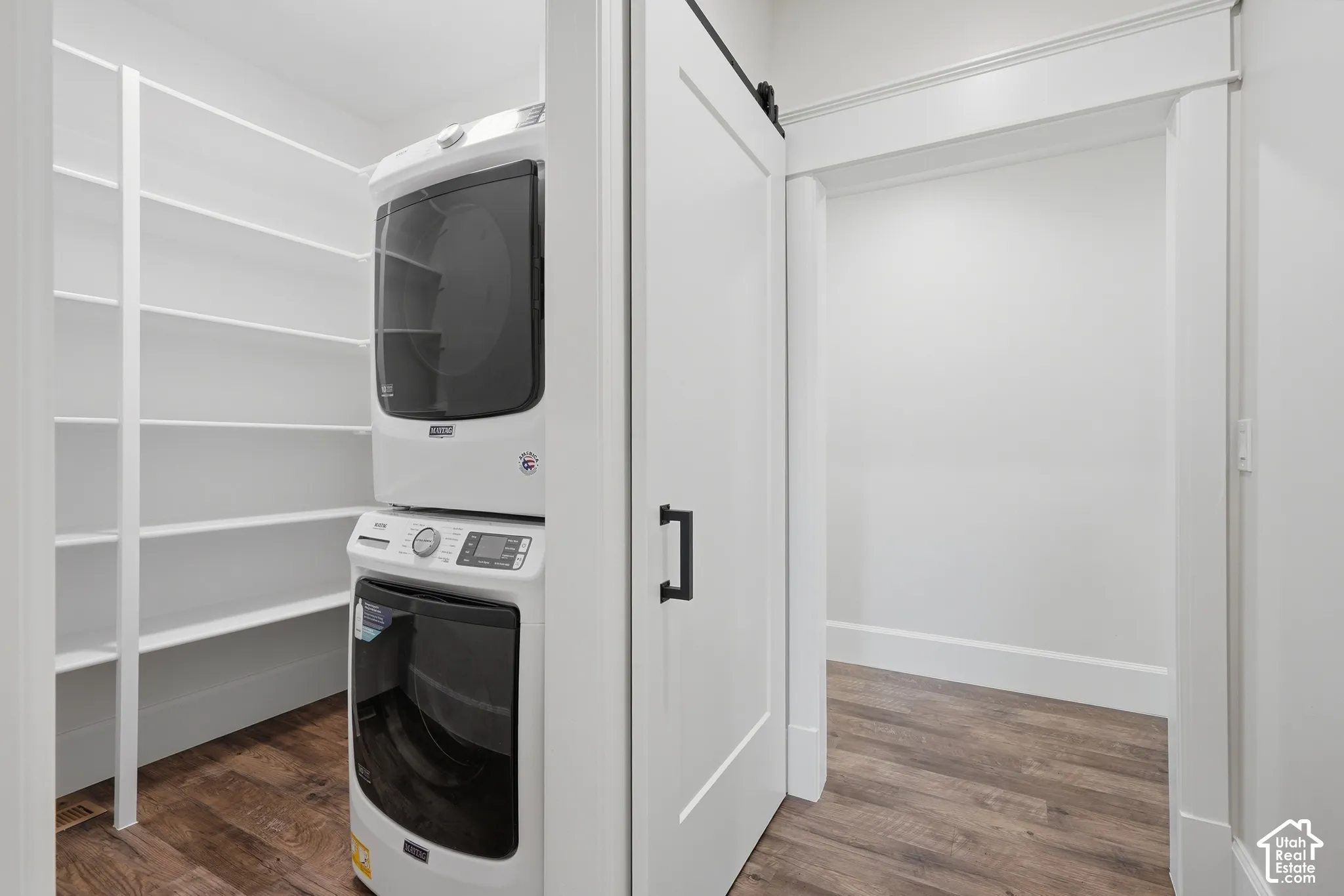 White barn door with matte black hardware, wood-finish flooring, built-in shelving, and white baseboards