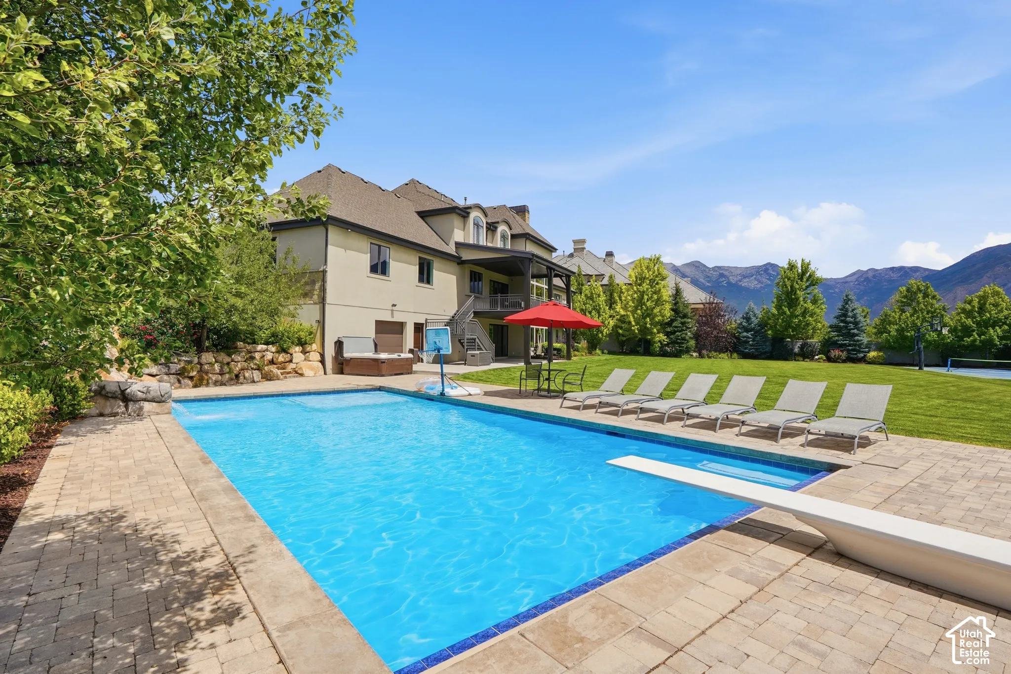 Expansive backyard featuring a large swimming pool with diving board, surrounding paver patio, and built-in spa