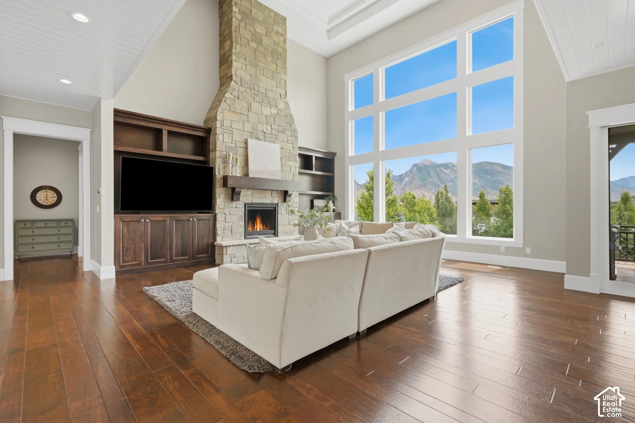 Expansive living space featuring a floor-to-ceiling stone fireplace, large built-in shelving, rich wood-finish flooring, and a soaring window wall showcasing mountain scenery