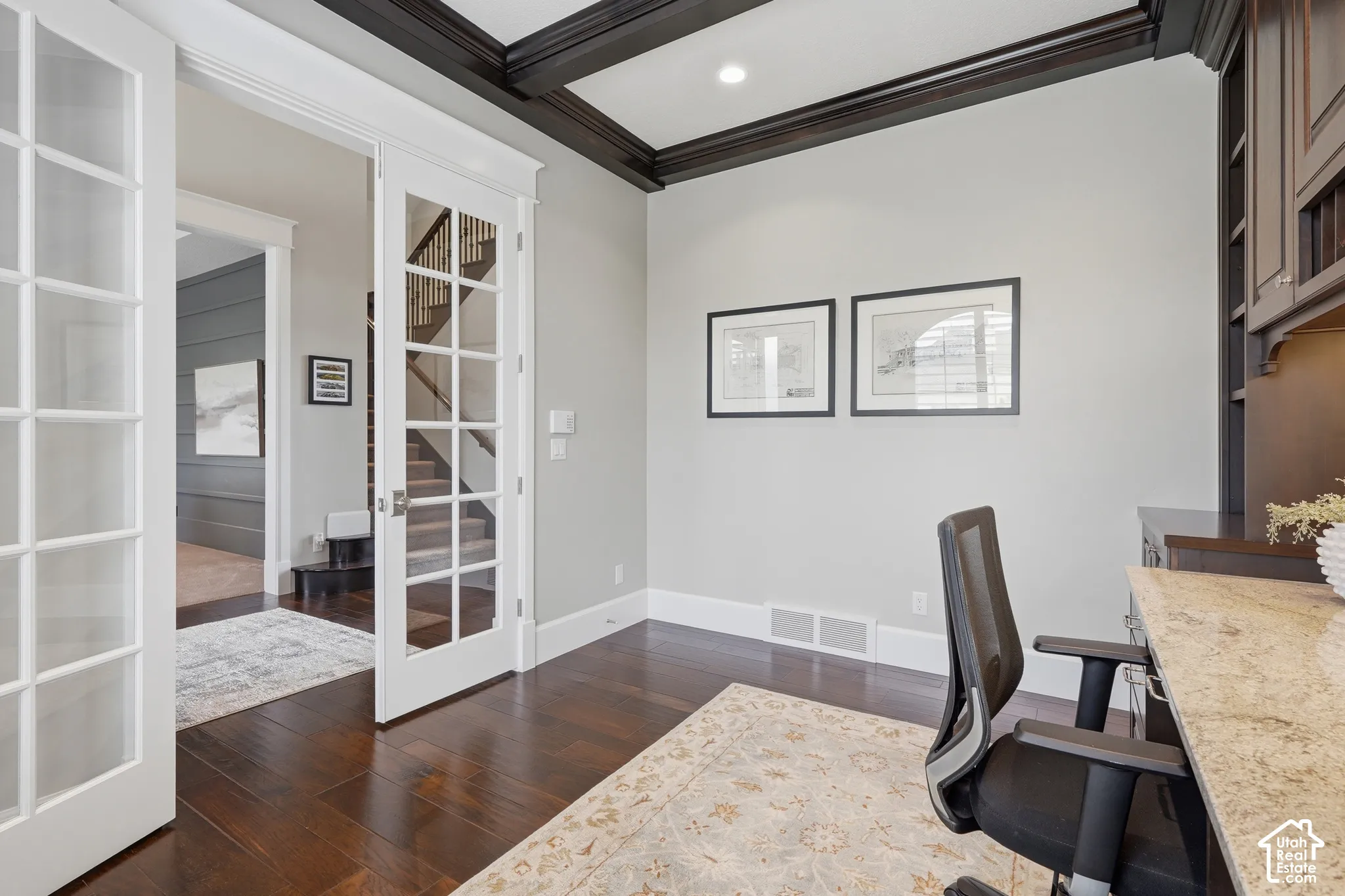 Dark wood-finish flooring, white French doors, coffered ceiling, built-in cabinetry, and a granite-finish countertop