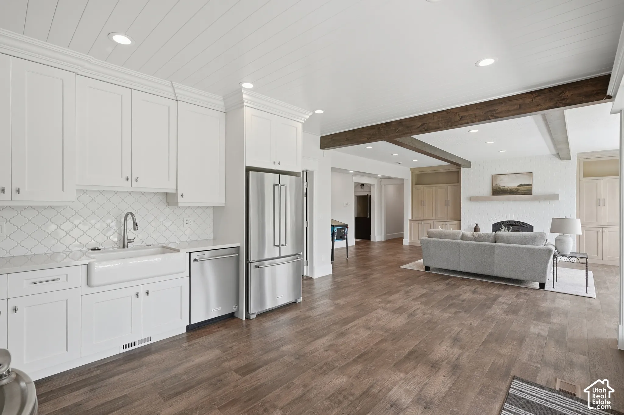 Kitchen area featuring white shaker-style cabinetry, a farmhouse sink, stainless steel appliances, and a patterned tile backsplash