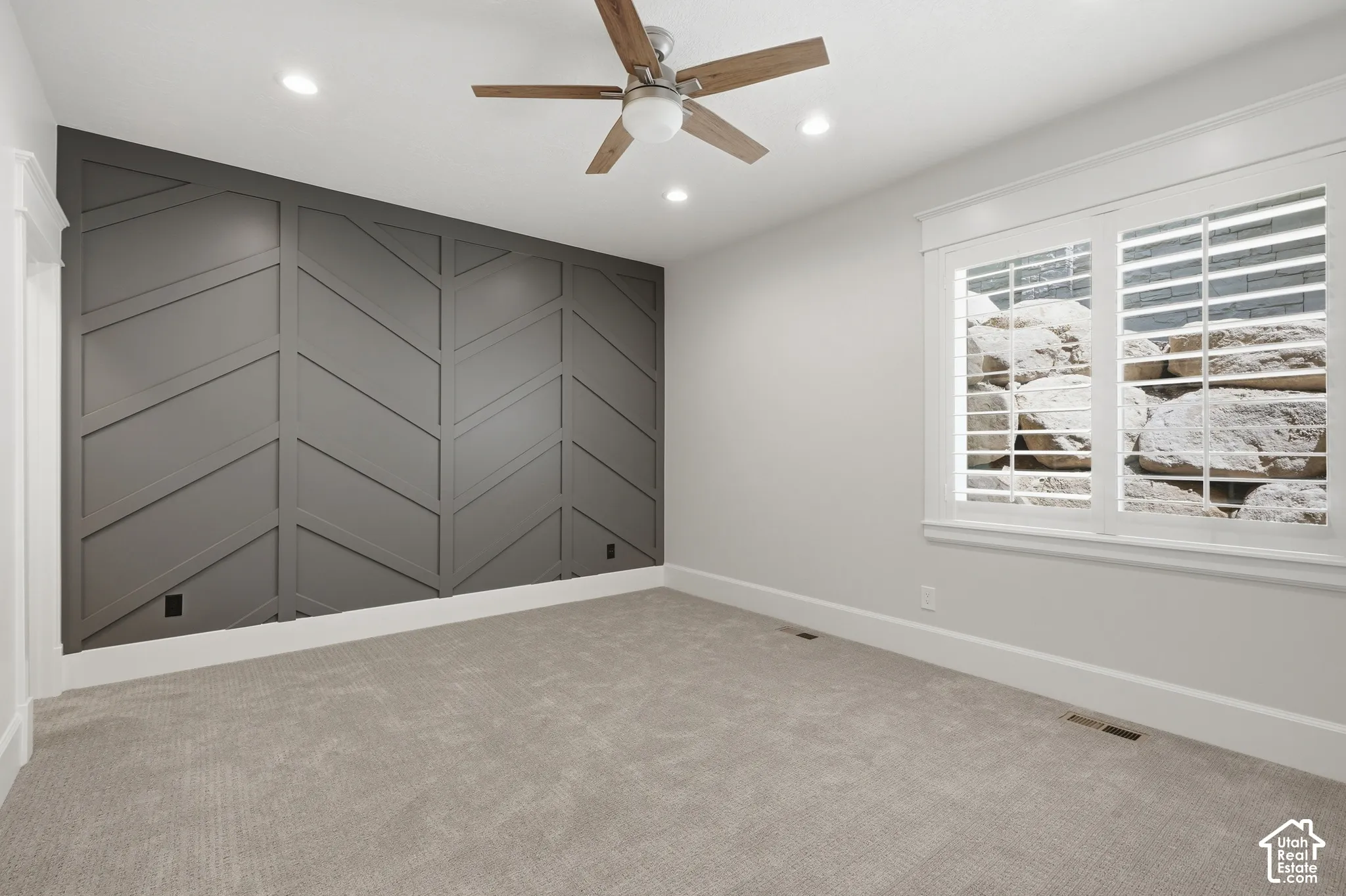 Accent wall with geometric paneling, recessed lighting, ceiling fan with wood-finish blades, and carpeted flooring