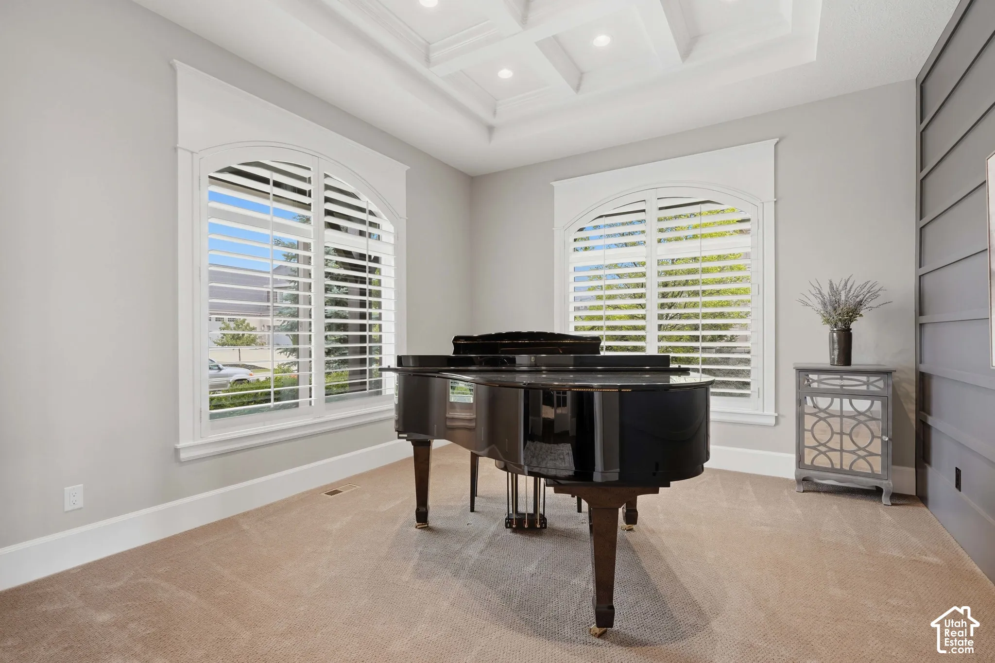 Arch-top windows with custom plantation shutters, coffered ceiling with recessed lighting, and a neutral carpeted floor
