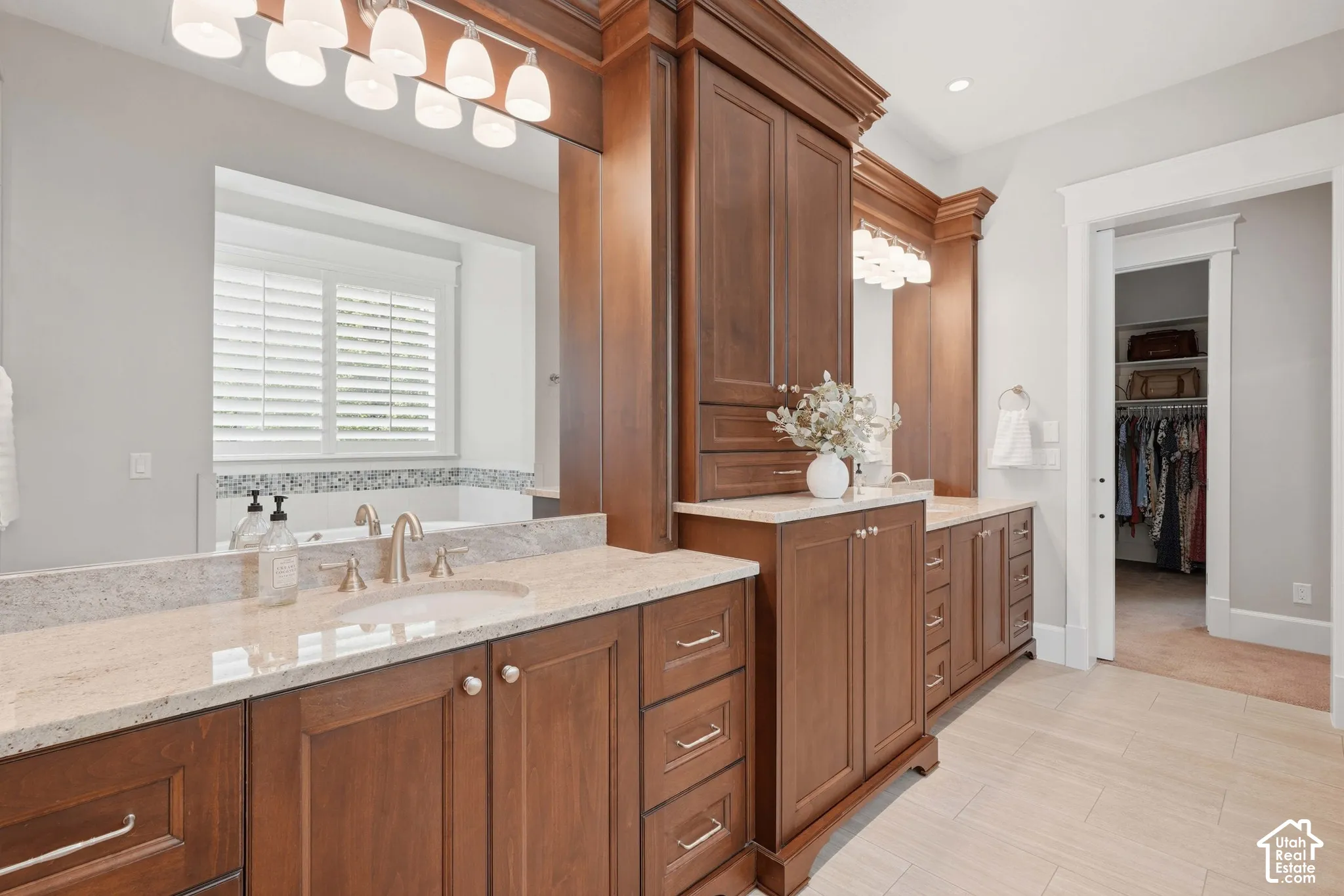 Dual vanity with integrated sinks, expansive wood cabinetry, light-toned countertops, and light tile flooring