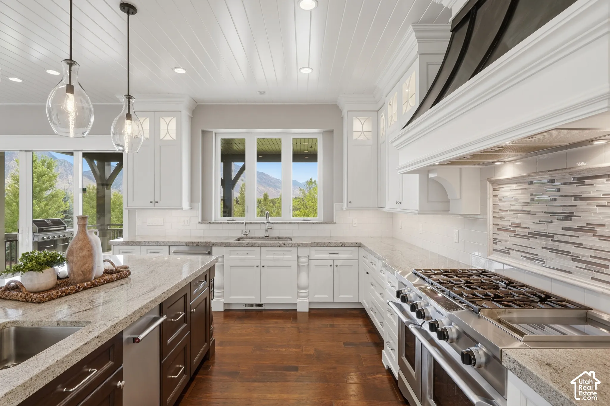 Kitchen featuring wood-finish flooring, white cabinetry, integrated stainless steel appliances, a large center island with an undermount sink, and pendant lighting