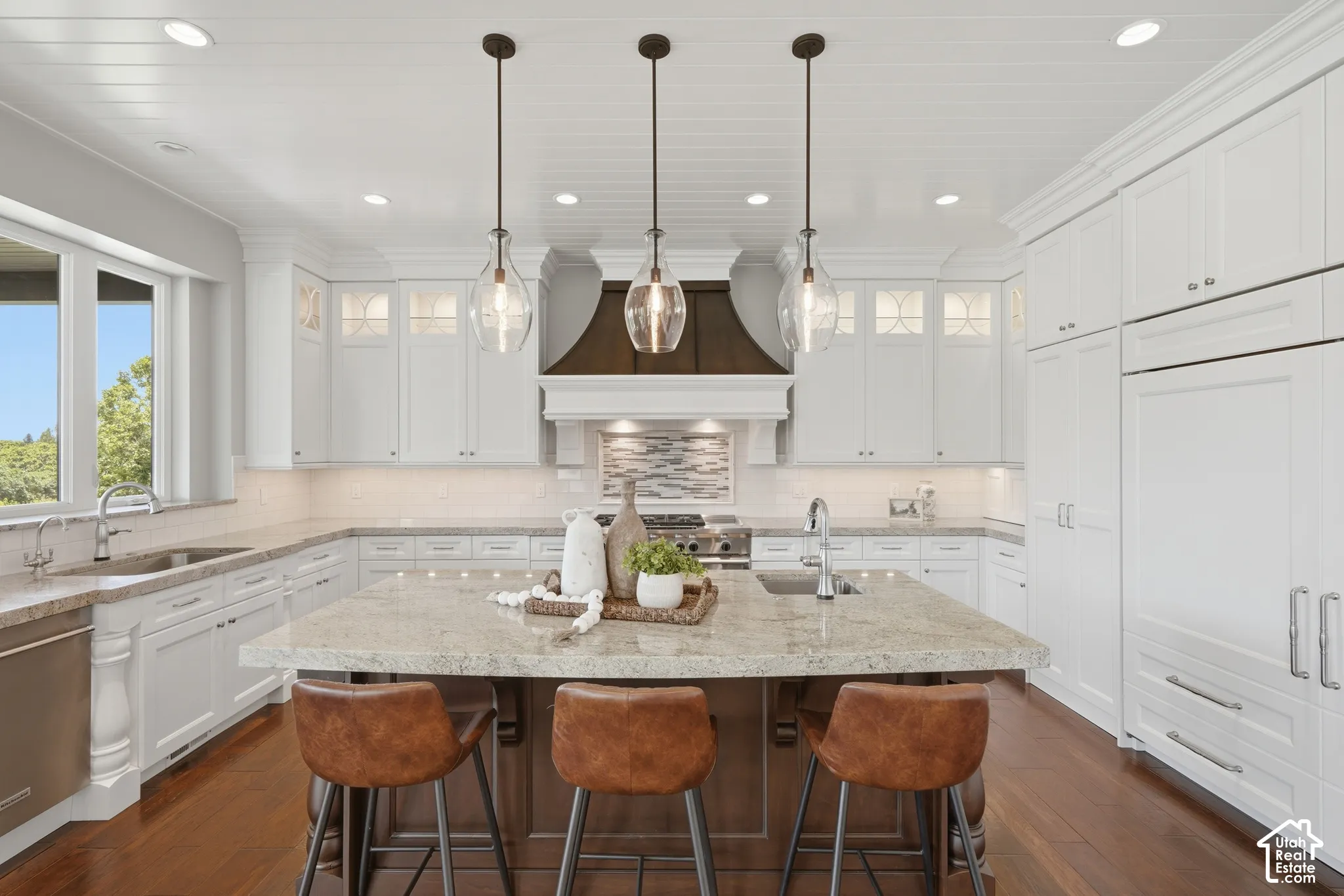 Spacious kitchen featuring white cabinetry, light-toned countertops, a central island with integrated sink, stainless steel appliances, and dark wood-finish flooring