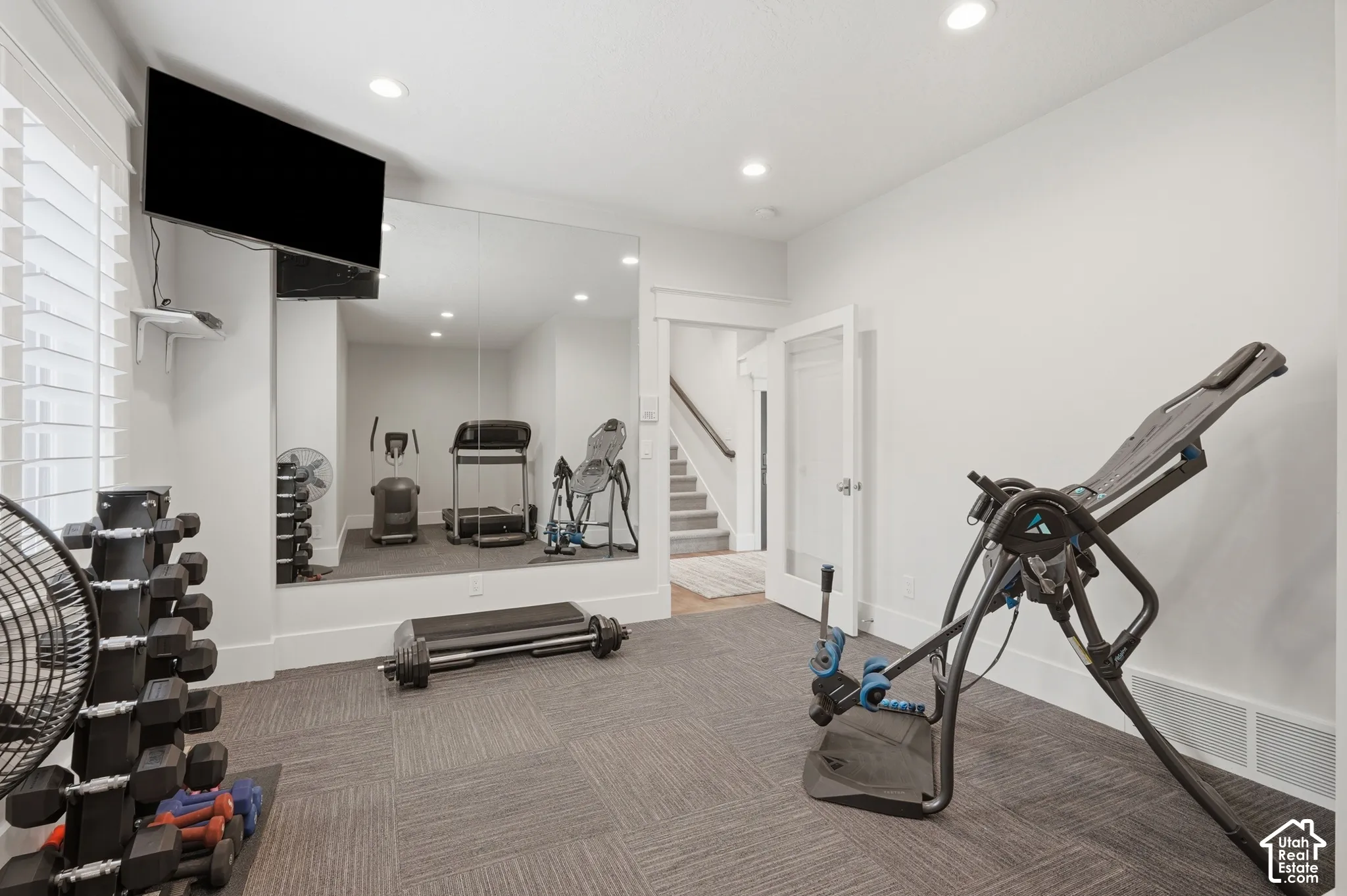 Recessed lighting illuminates this space featuring wall-to-wall mirrors, light-colored walls, and patterned carpet tiles