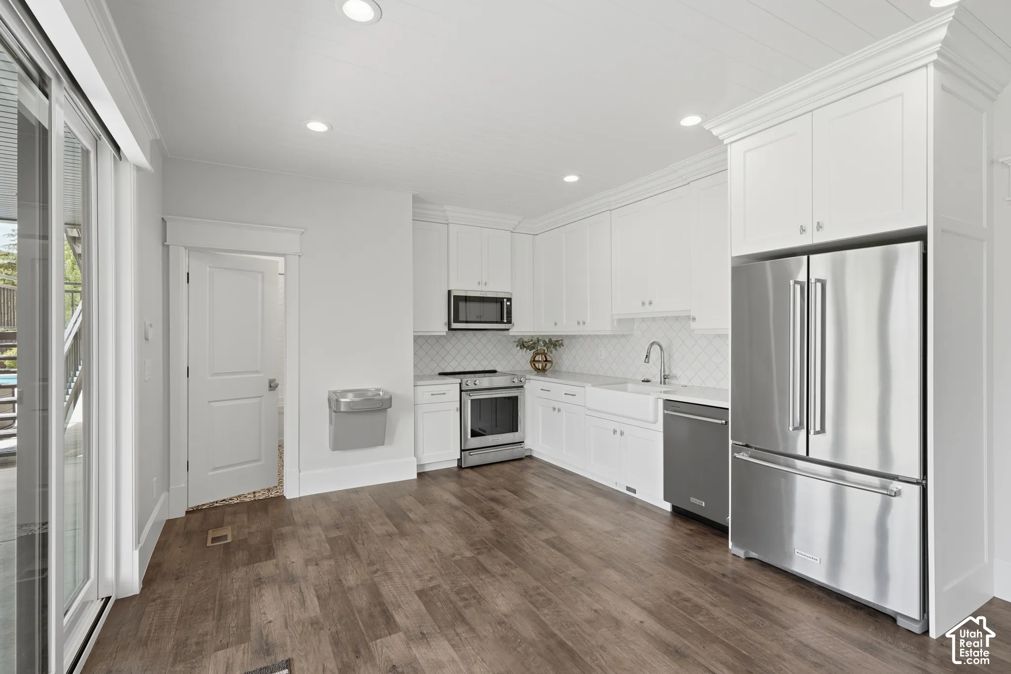 Spacious kitchen featuring wood-finish flooring, white cabinetry, stainless steel appliances, and a white farmhouse sink