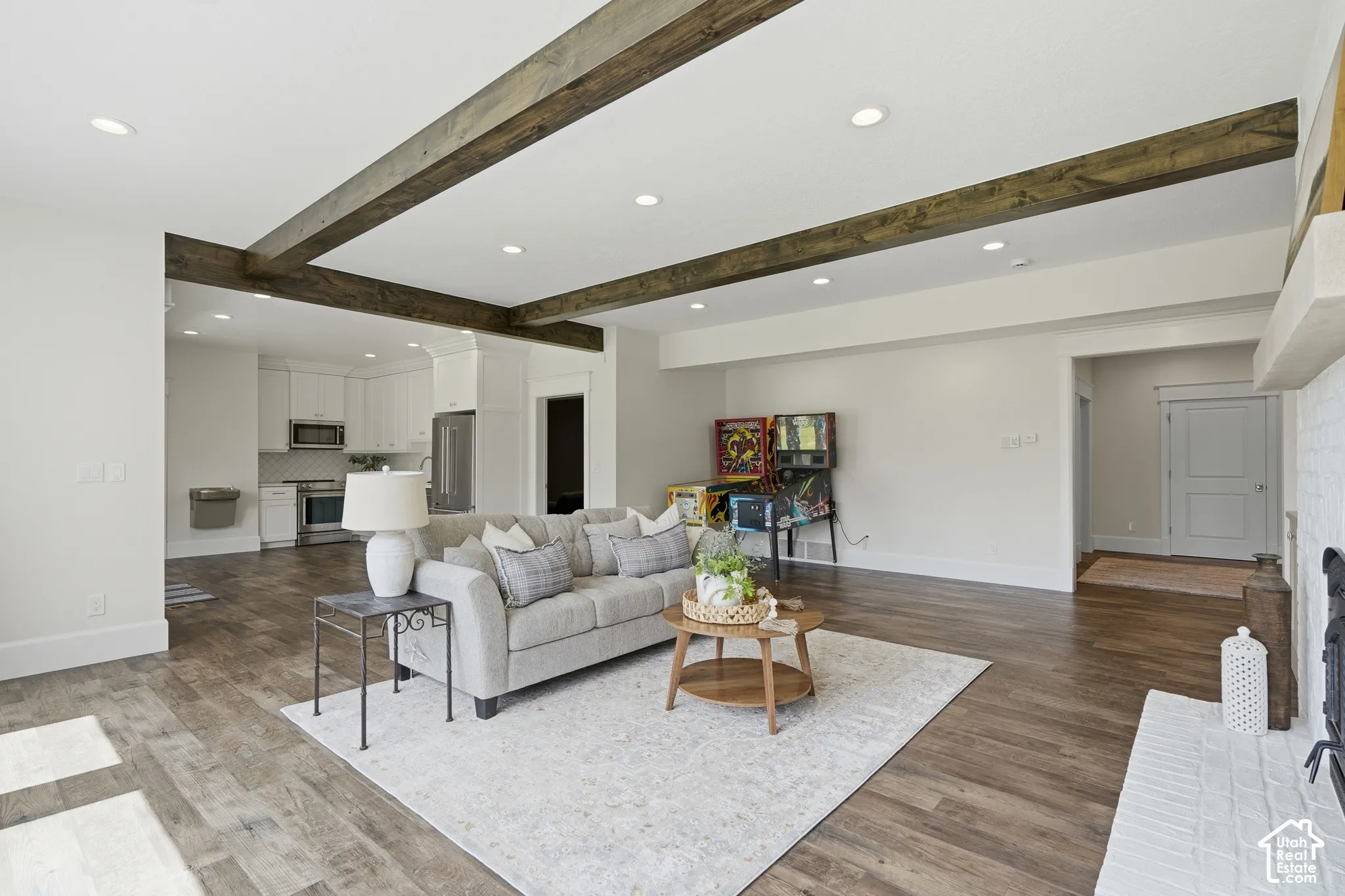 Spacious living area featuring wood-finish flooring, recessed lighting, exposed ceiling beams, and a white brick fireplace