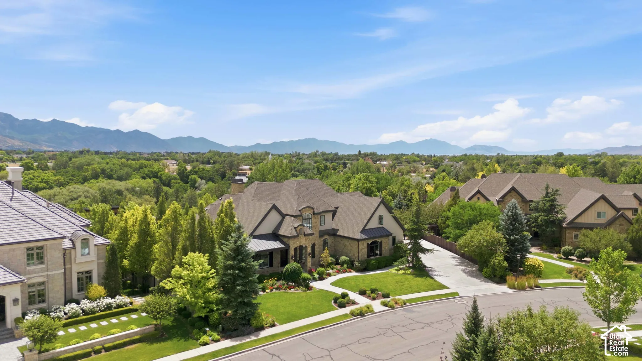 Stucco and stone exterior with a multi-gabled roof, mature landscaping, and a paved driveway