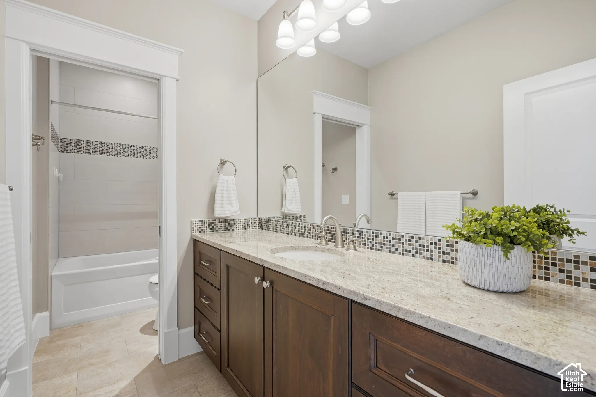 Bathroom featuring a single vanity with dark wood-finish cabinetry, a light-toned countertop, and a mosaic tile backsplash