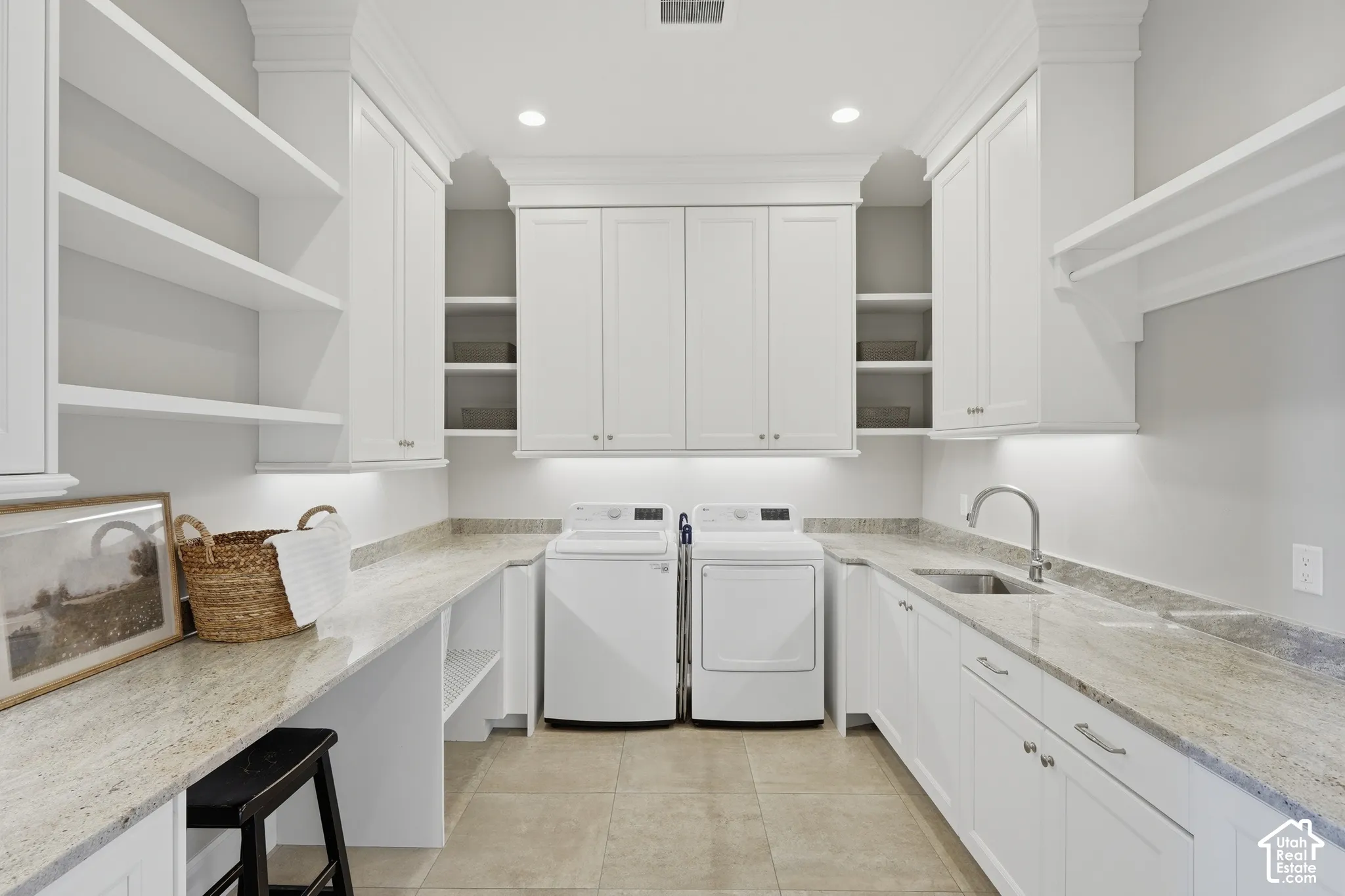 White shaker-style cabinetry, light-toned stone countertops, undermount sink with a gooseneck faucet, integrated shelving, and tile flooring