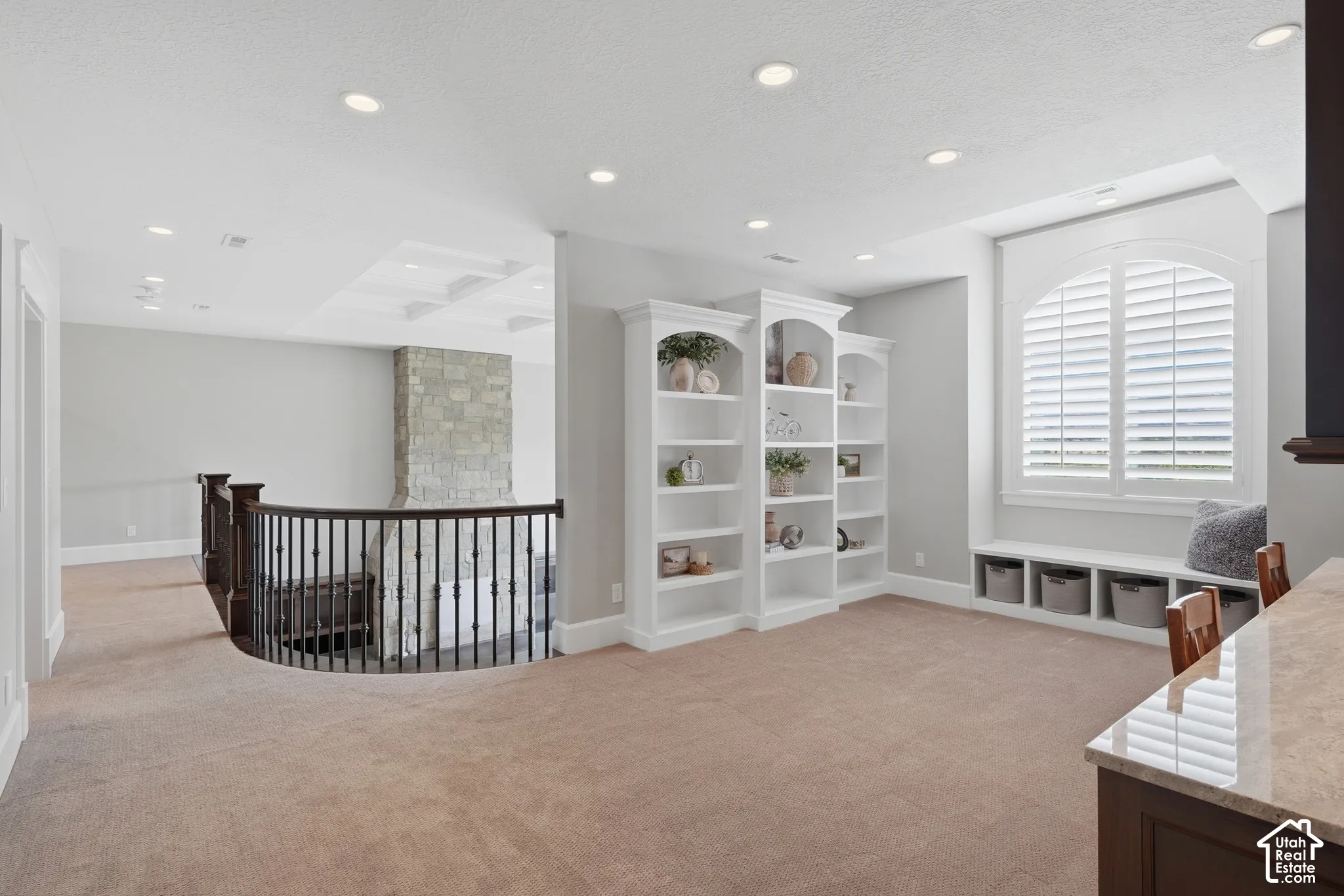 Built-in shelving, arched window with plantation shutters, window seat with integrated storage, coffered ceiling, and stone-clad fireplace