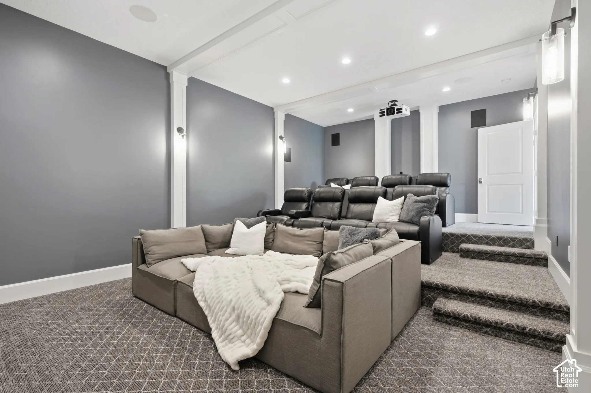 Carpeted tiered seating, integrated ceiling speakers, recessed lighting, wall sconces, and a ceiling-mounted projector
