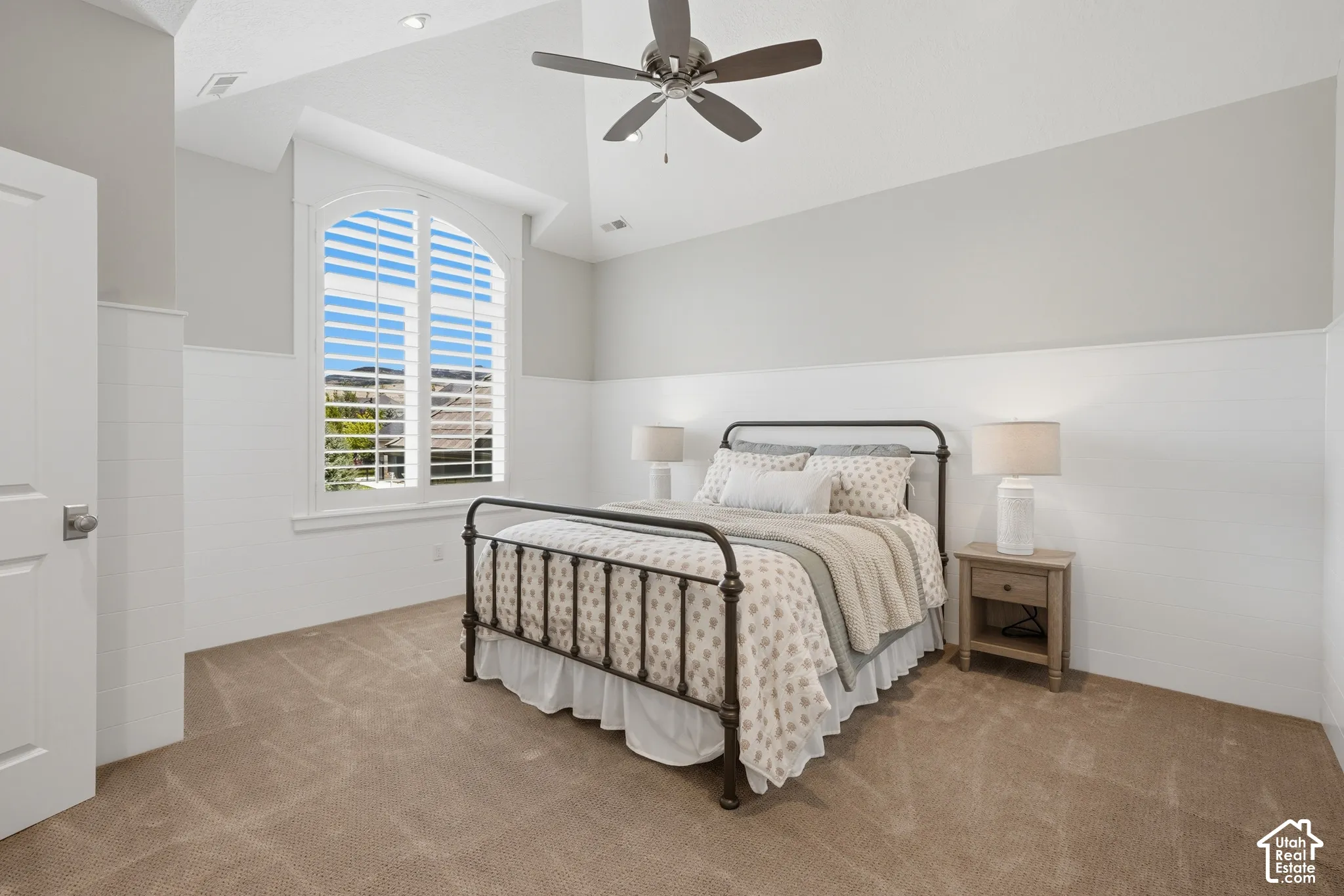 Arched window with plantation shutters, vaulted ceiling, ceiling fan, recessed lighting, and wall paneling