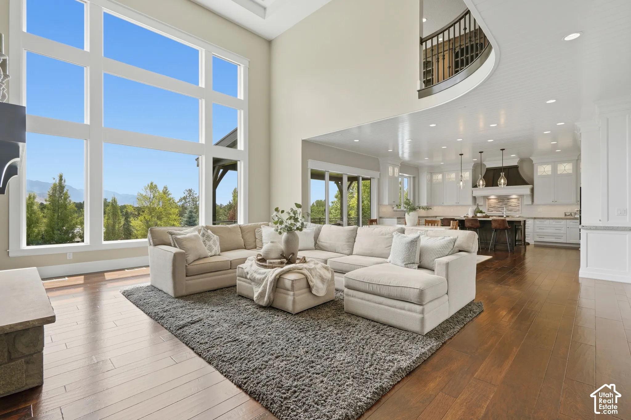 Great room featuring expansive windows, wood-finish flooring, a two-story ceiling, a stone-clad fireplace, and an open concept to the kitchen