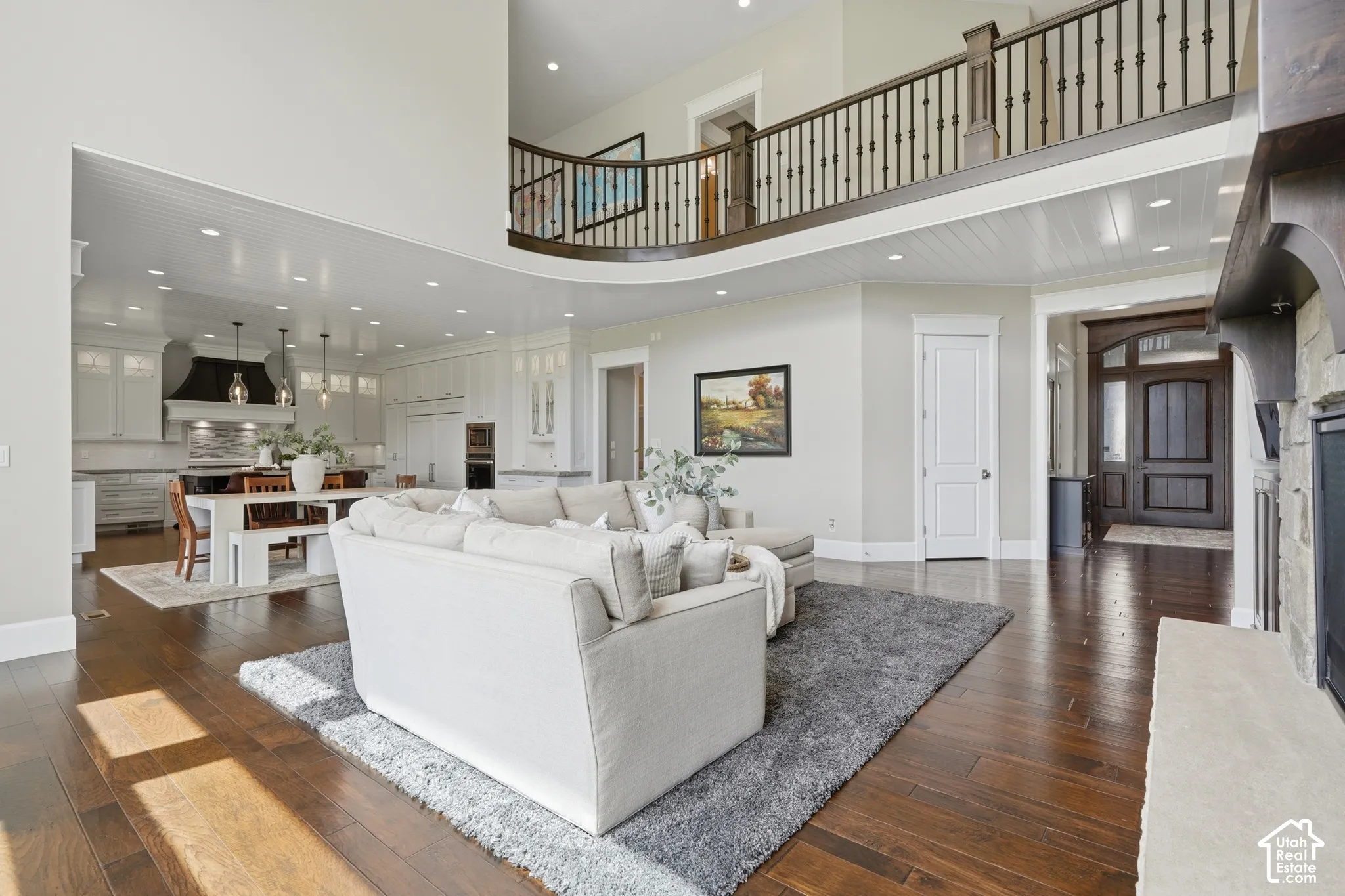 Great room with wood-finish flooring, a stone-surround fireplace, and a second-story overlook with an ornate railing