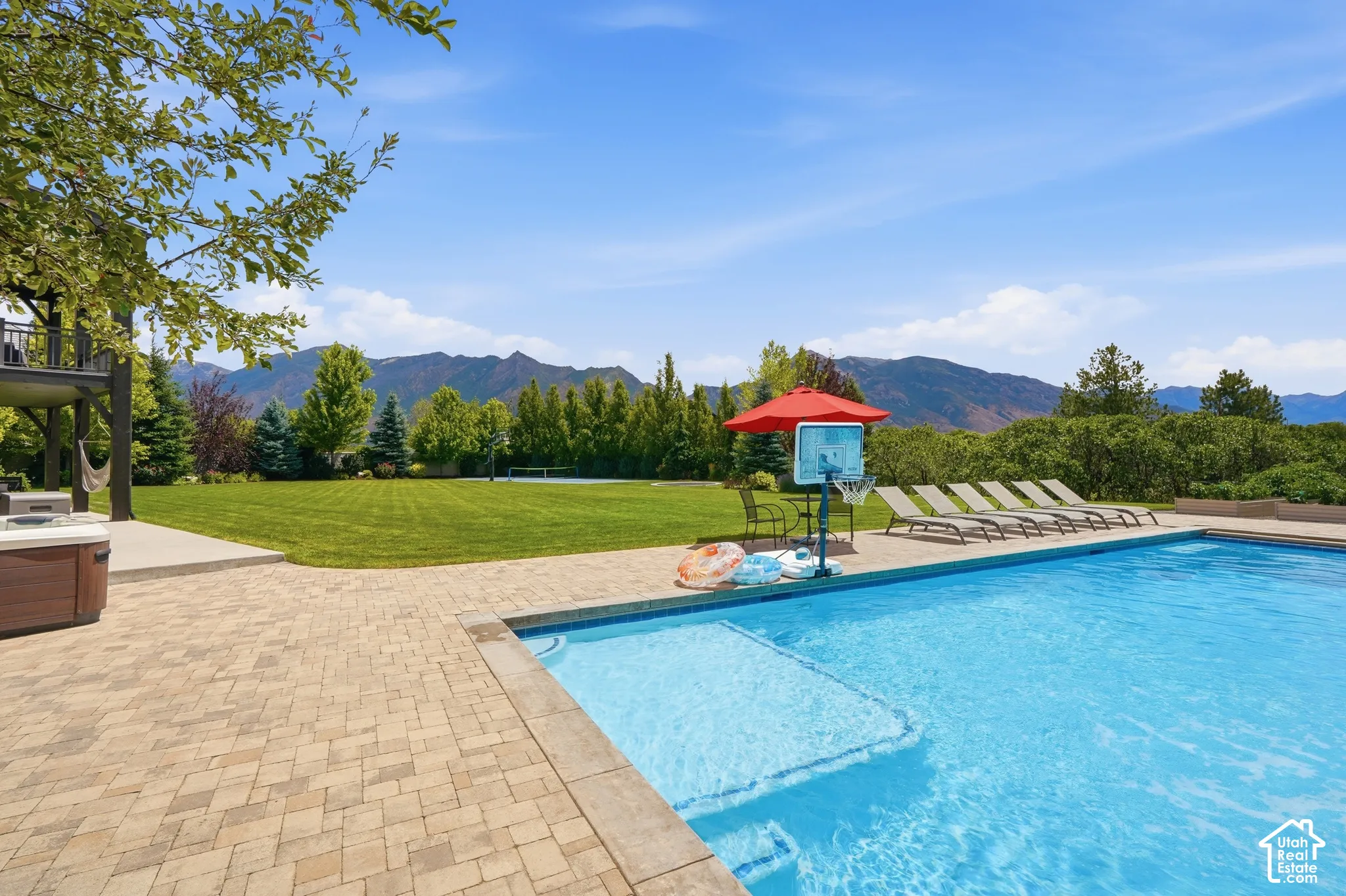 Expansive outdoor living area featuring a rectangular swimming pool, paver patio, and an integrated hot tub