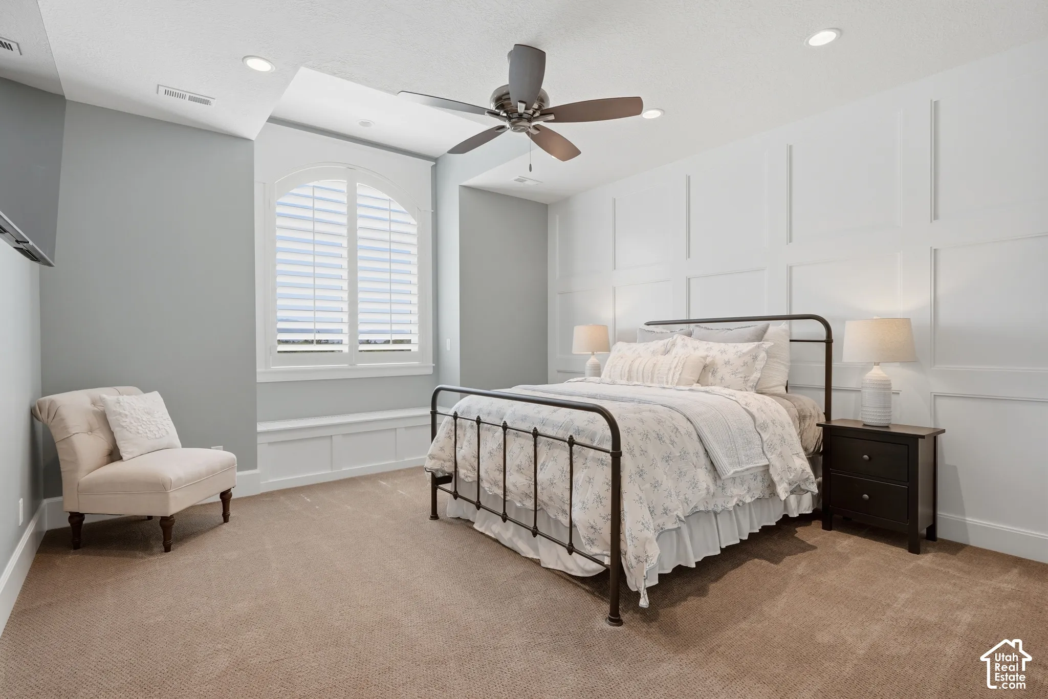 Arched window with plantation shutters, integrated window bench, ceiling fan, recessed lighting, and accent wall paneling