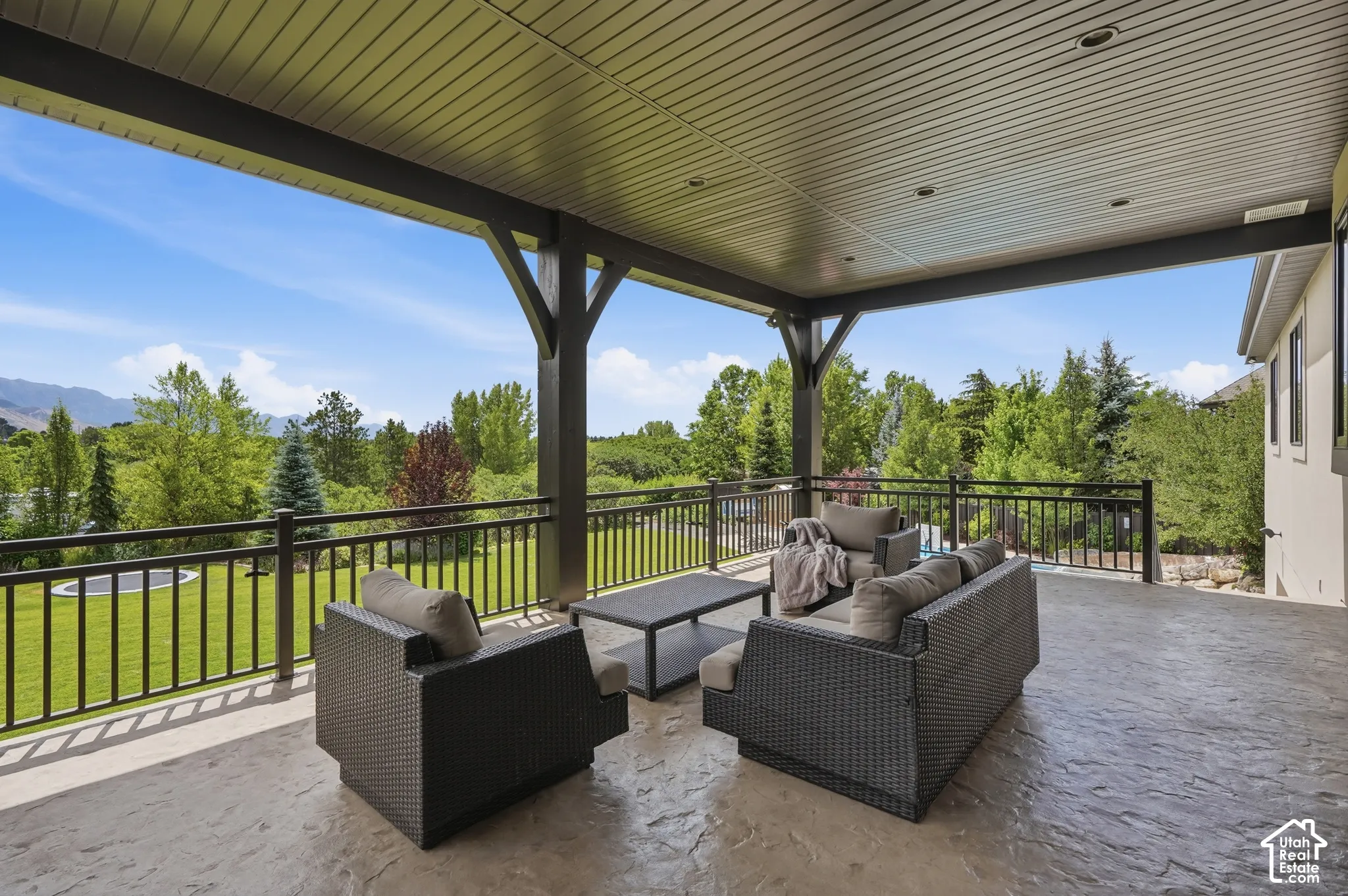 Covered patio with stamped concrete flooring, supported by dark wood beams, and framed by a black metal railing