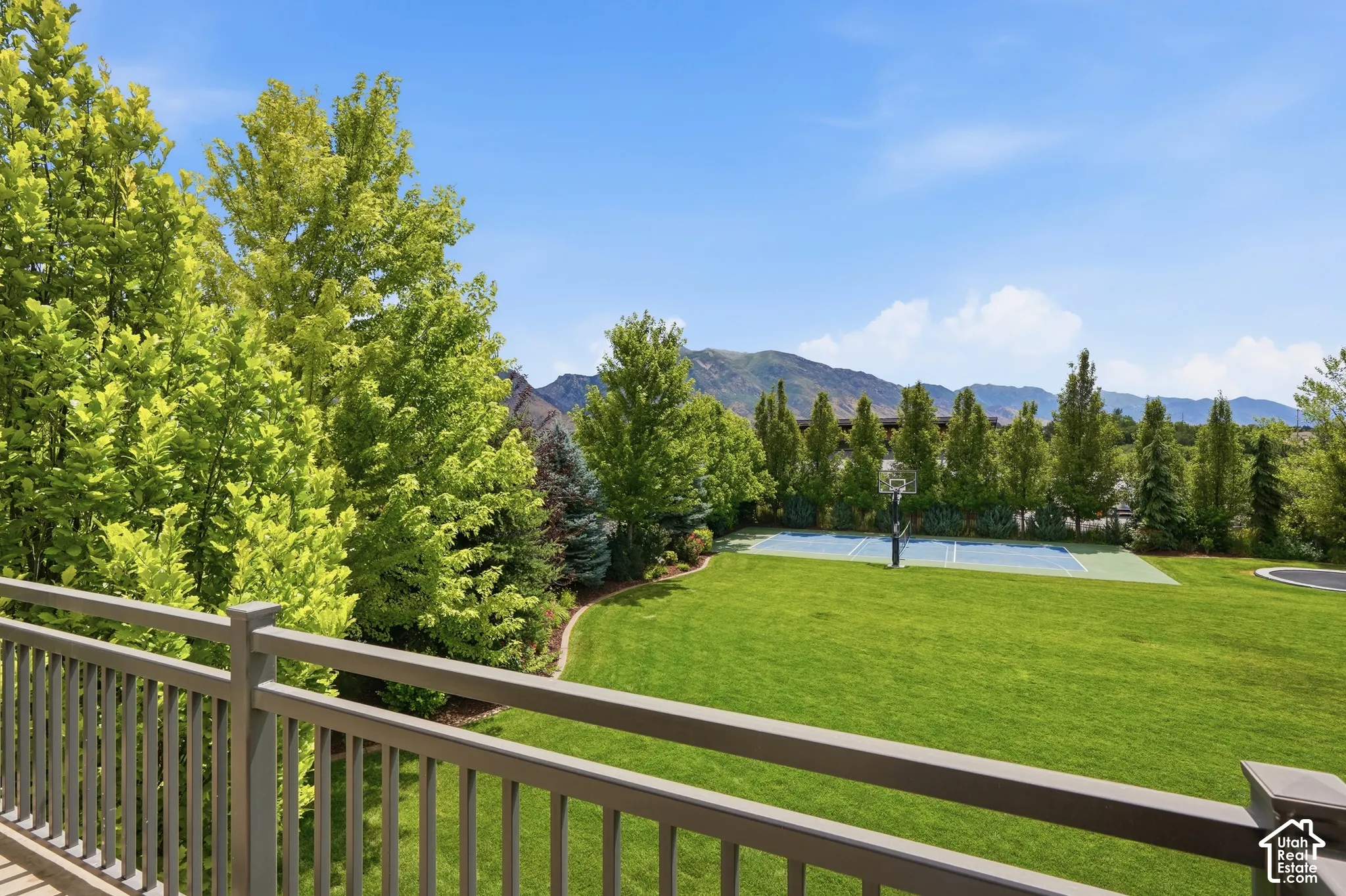 Expansive green lawn with a dedicated sports court, mature trees, mountain backdrop, and a balcony with a gray railing