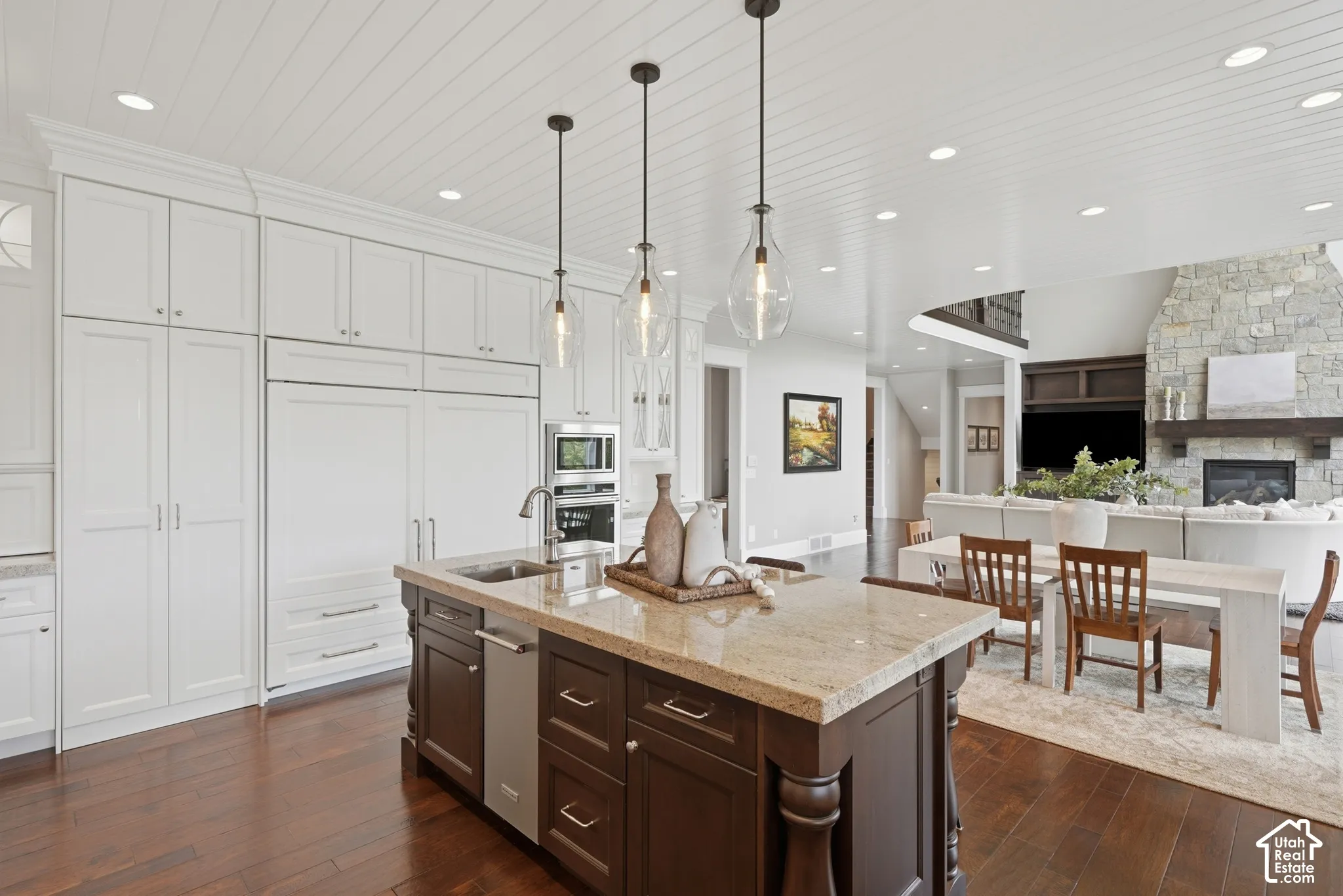 Kitchen island with a light-toned countertop, dark wood-finish cabinetry, and three pendant lights
