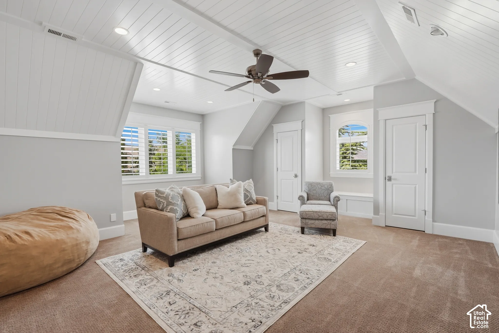 Sloped ceilings with paneling, recessed lighting, ceiling fan, window with white plantation shutters, and built-in window bench