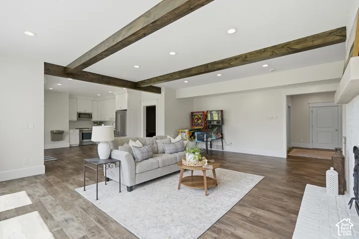 Spacious living area featuring wood-finish flooring, recessed lighting, exposed ceiling beams, and a white brick fireplace