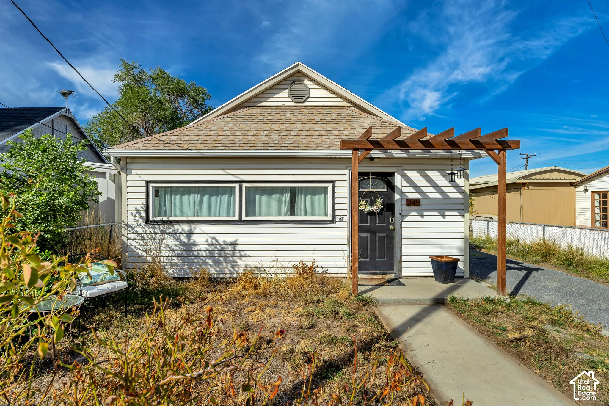 White horizontal siding exterior with a dark entry door and decorative pergola
