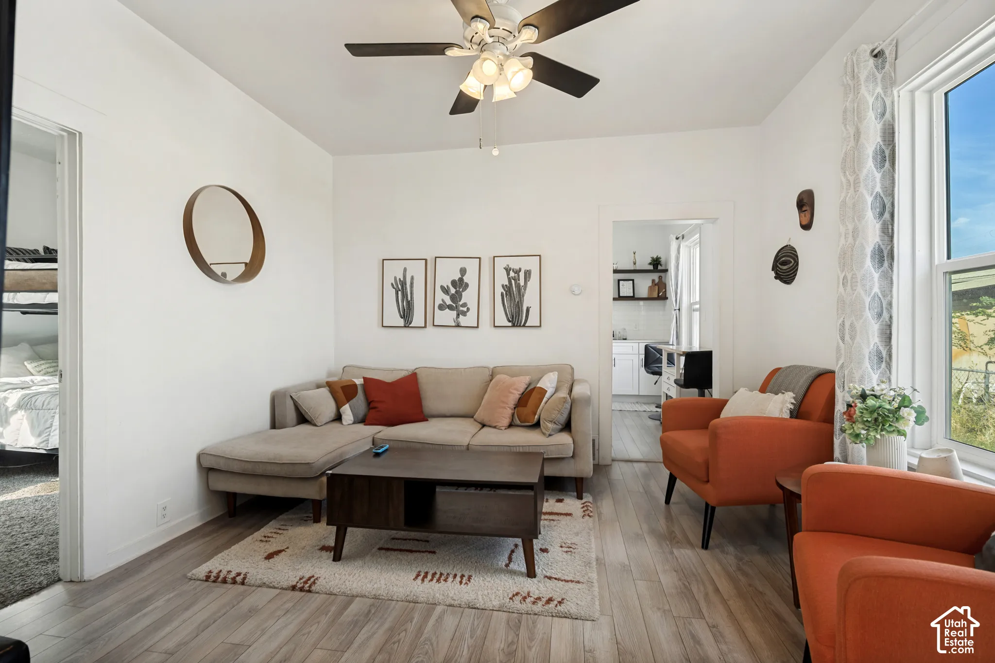 Wood-finish flooring throughout, white walls, ceiling fan with integrated lighting, and multiple windows for natural illumination