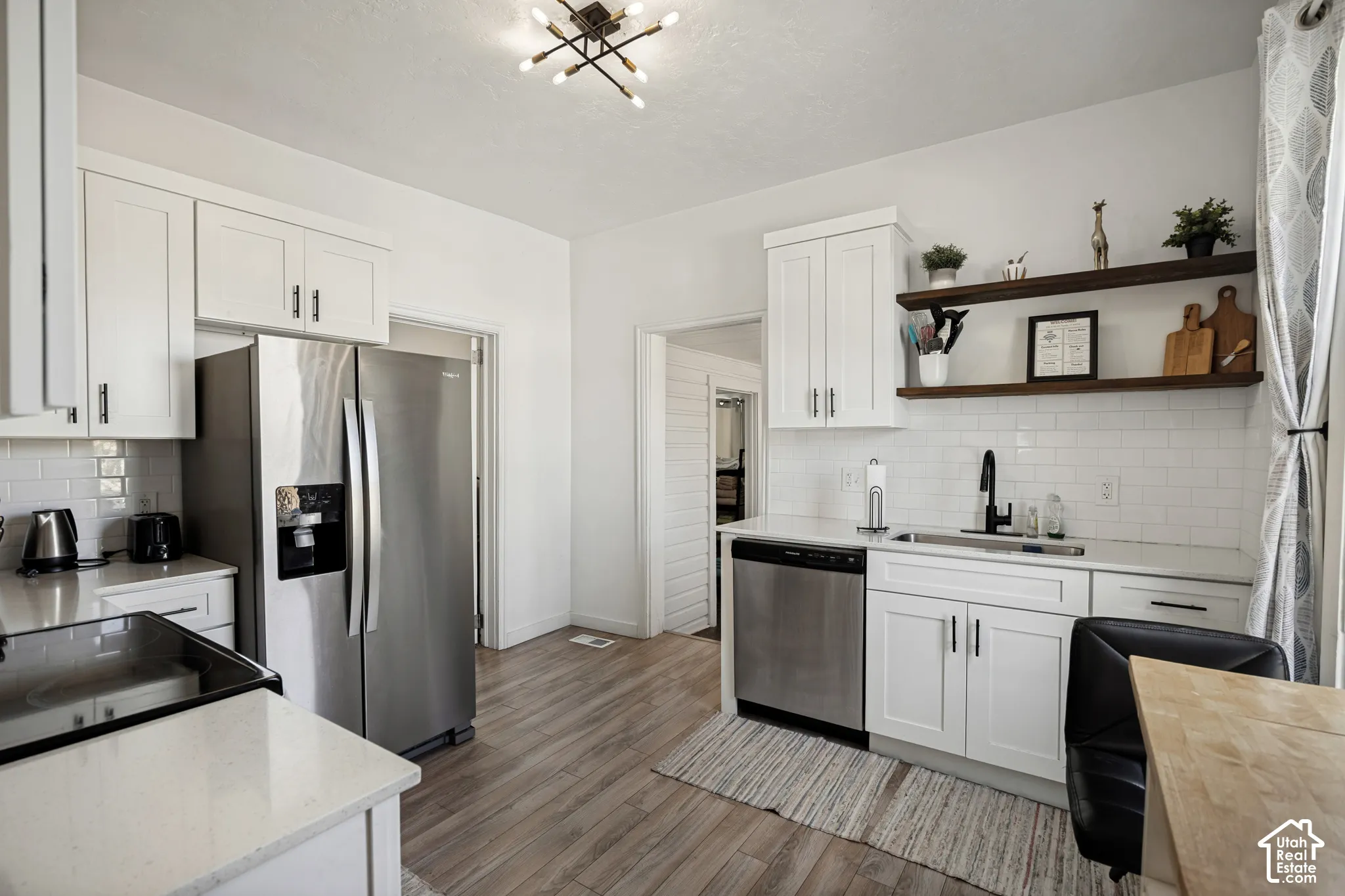 Kitchen featuring white shaker cabinetry, stainless steel appliances, wood-finish flooring, white subway tile backsplash, and a modern ceiling light fixture