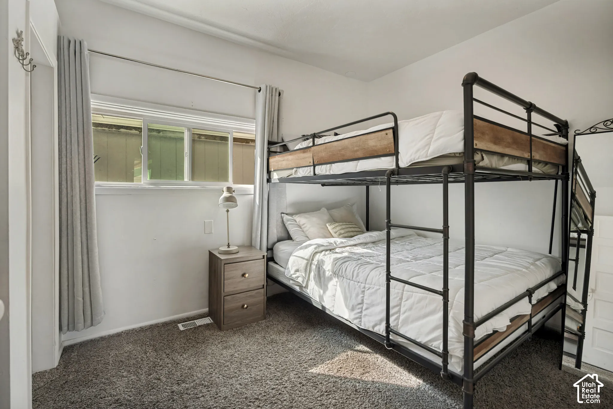 Carpeted flooring, white walls, and a window with blinds and curtains