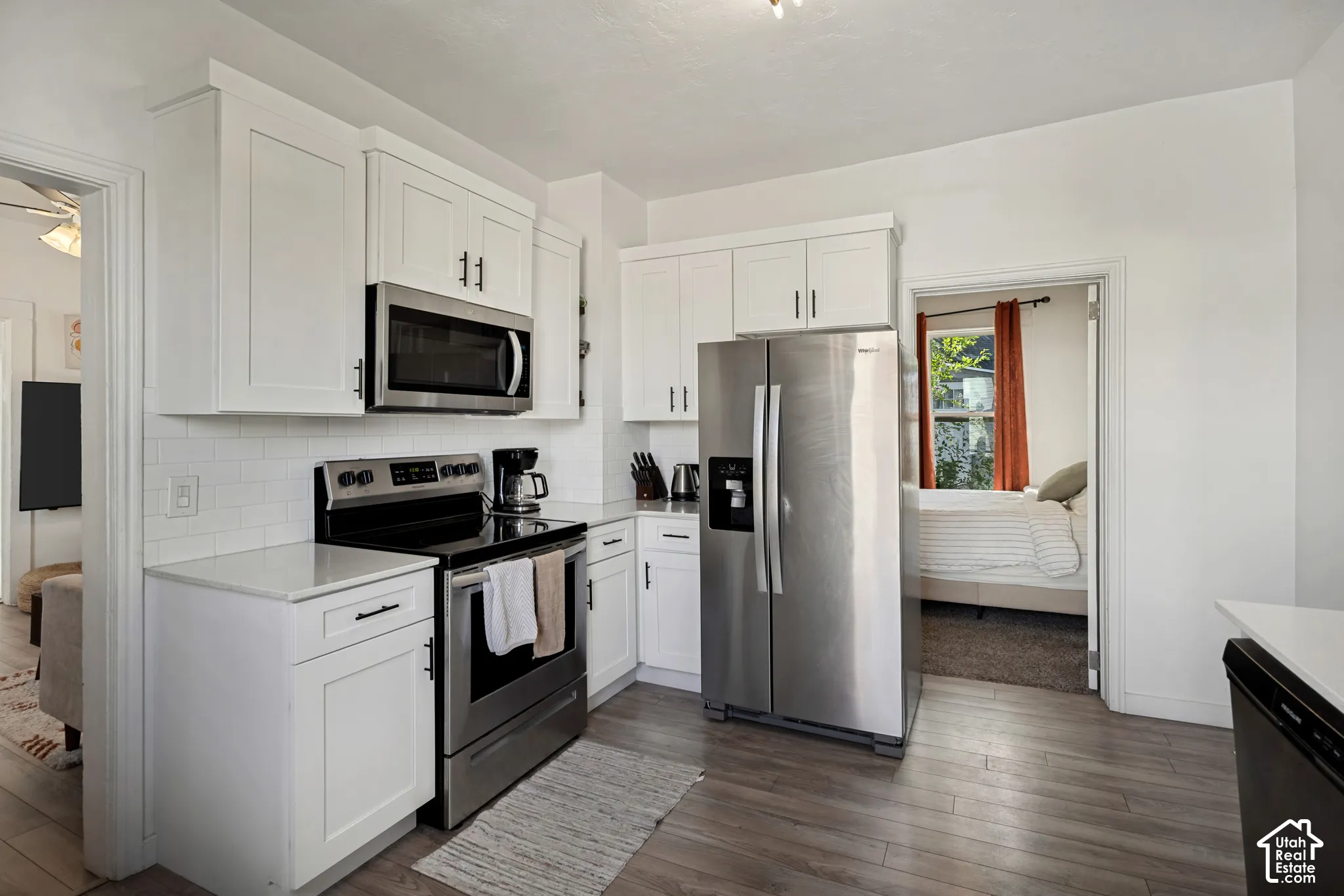 Kitchen featuring white shaker-style cabinetry, stainless steel appliances, a subway tile backsplash, and wood-finish flooring