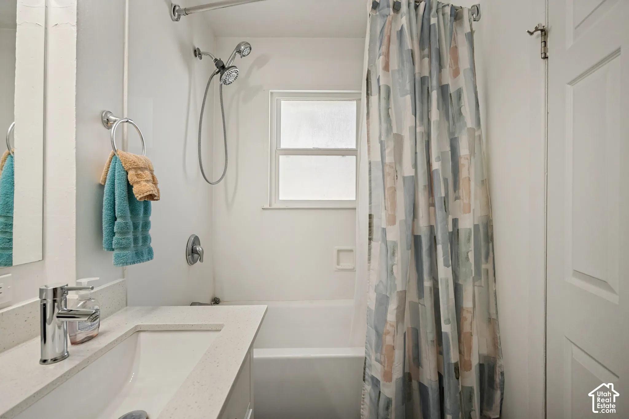 Bathtub with integrated shower head, white vanity with integrated sink, polished chrome faucet, and small window with privacy glass