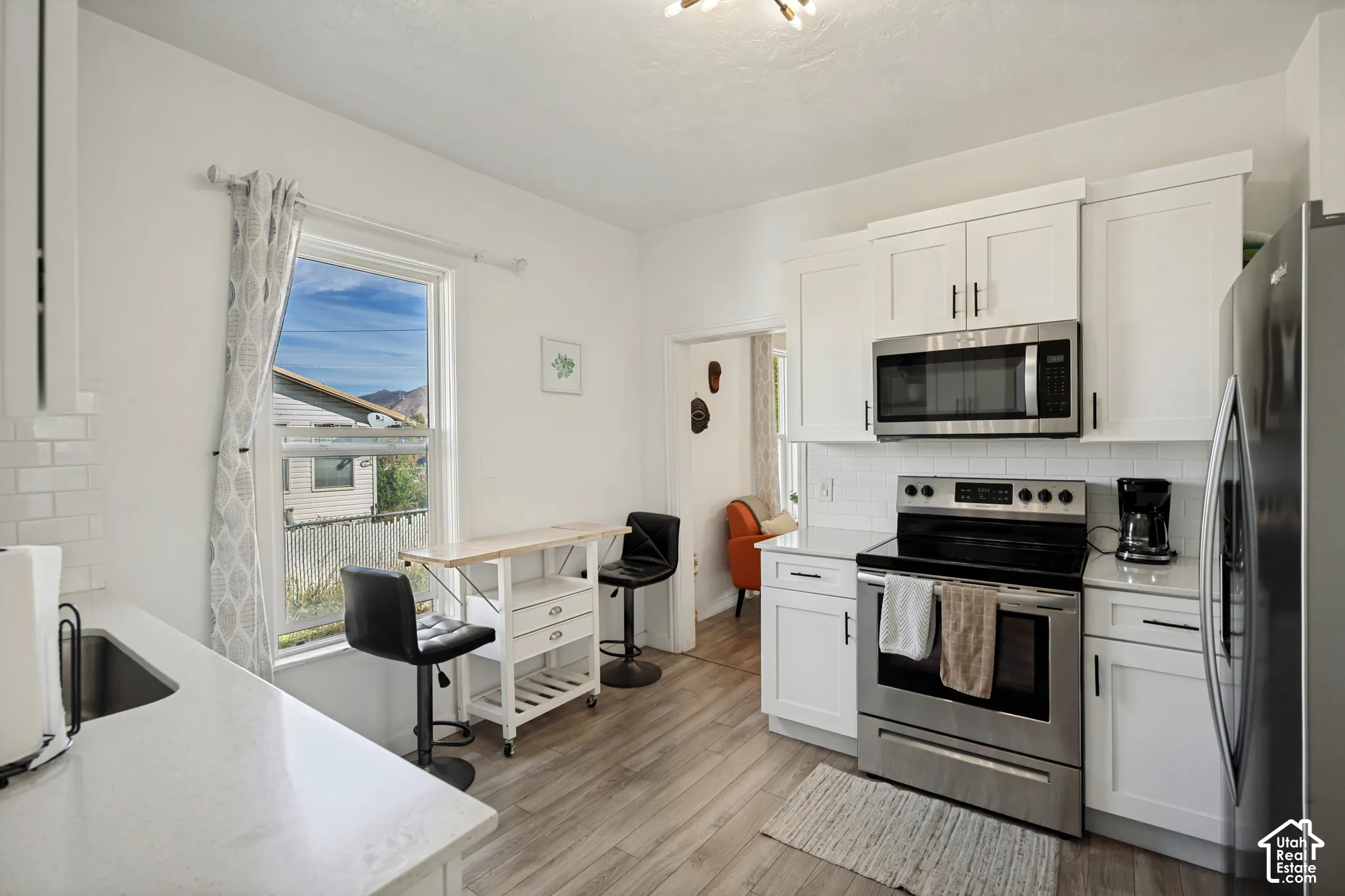 White shaker-style cabinetry with matte black hardware, stainless steel appliances, subway tile backsplash, light-toned countertops, and wood-finish flooring