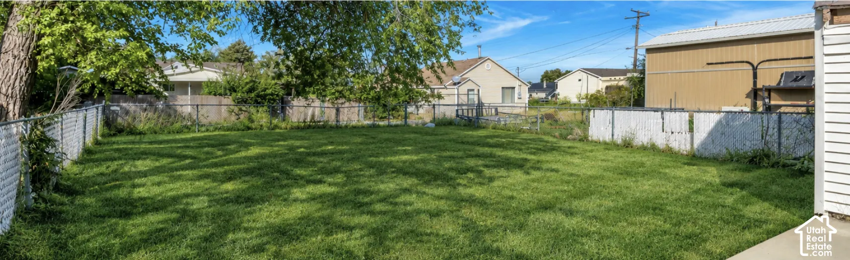 Expansive green lawn with mature tree, partially enclosed by a chain link fence
