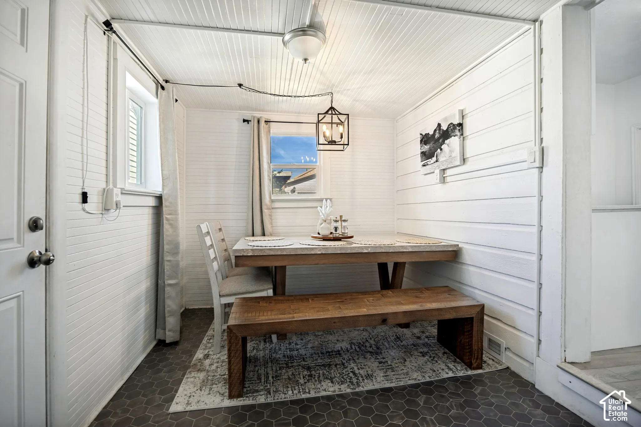 Hexagonal floor tiling, horizontal plank wall finishes, beadboard ceiling, a window with curtains, and a black metal chandelier