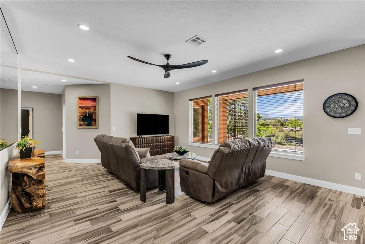 Sloped ceiling with recessed lighting, modern ceiling fan, wood-finish flooring, and multiple windows