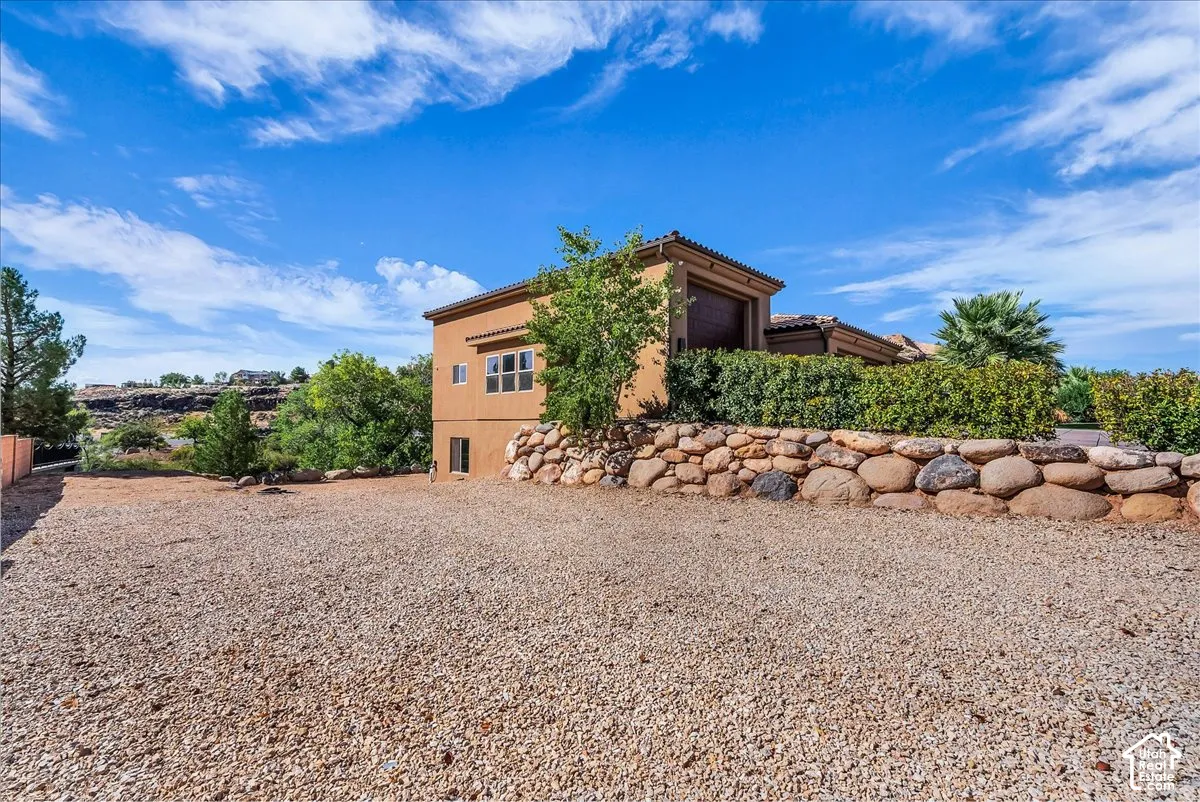 Stucco exterior with multiple windows, complemented by a stone retaining wall and lush landscaping