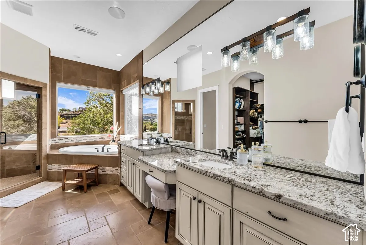 Spa-like bathroom with a built-in jetted tub, expansive window, tiled shower enclosure, dual vanity with undermount sinks, and stone countertops