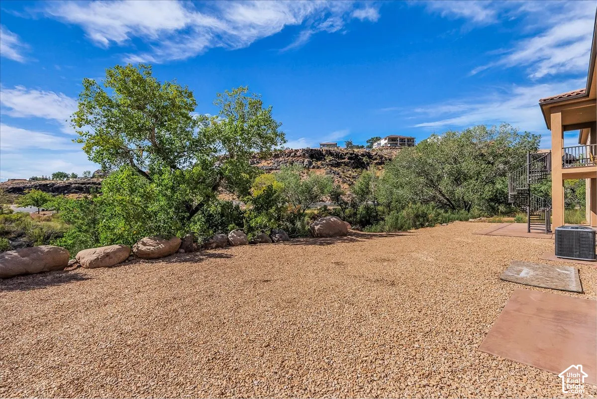 Expansive gravel hardscaping with a concrete pad, surrounded by mature trees and natural rock landscaping