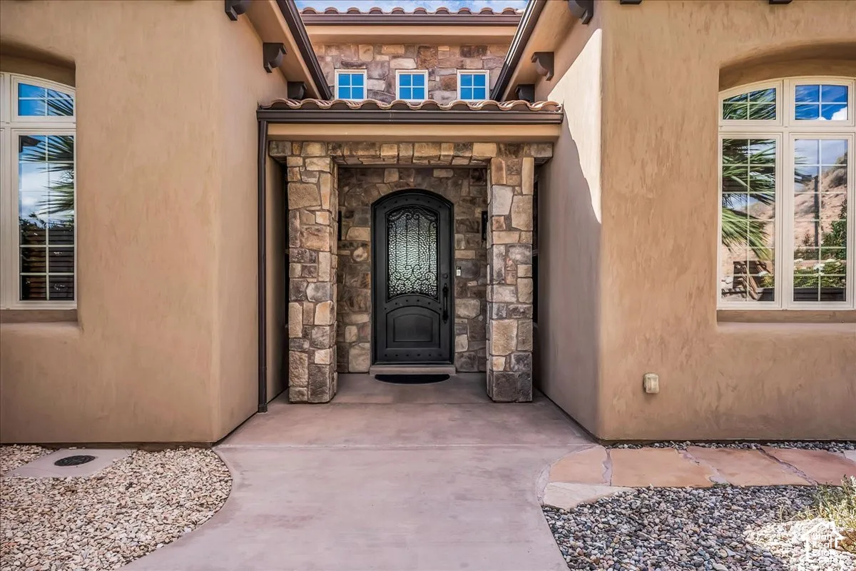 Stucco exterior with stone accents, arched entry, decorative iron door, transom windows, and tile roof