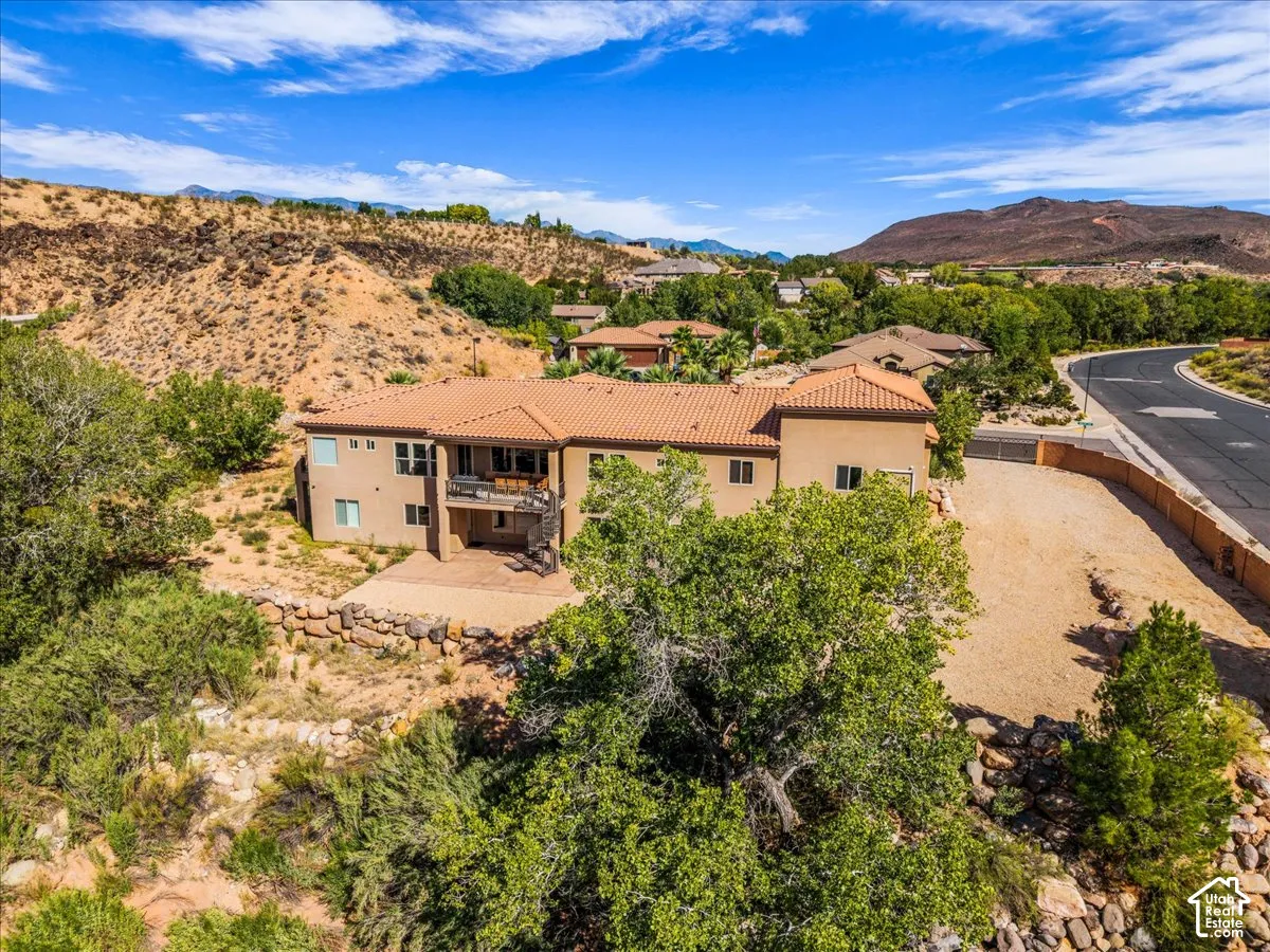Terracotta tile roof, stucco exterior, upper-level balcony, lower-level patio, and natural landscaping with mature trees